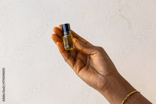 Close-up of a female hand holding a small 3ml glass roll-on Attar perfume oil bottle. Traditional Middle Eastern scent, concentrated essential oil, luxury fragrance concept.