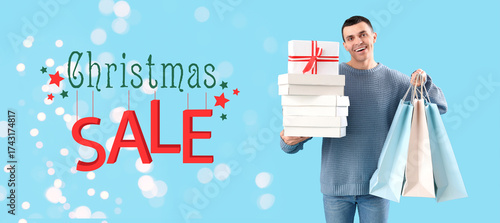 Handsome young happy man with gift boxes and shopping bags on blue background