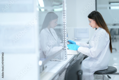 A pharmaceutical technician performs aseptic compounding inside a sterile biosafety cabinet, preparing a cell culture for biologic drug development under strict quality control conditions.