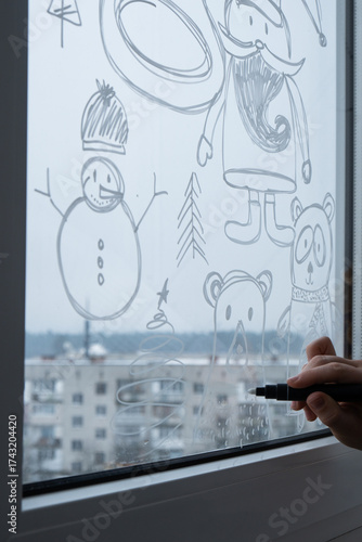 Sustainable responsible holiday decor. Female hand painting bear painted on window glass indoor at home. Christmas winter decoration. White pattern. Snow art tracery on season. Diy. Hygge home