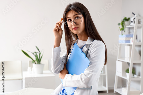 Thoughtful female doctor with clipboard in clinic
