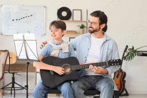 Cute boy learning guitar with private music teacher in room