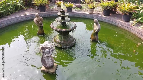 Video of a beautiful garden pond featuring a decorative fountain surrounded by artistic stone sculptures. The water flows gently, creating a calm and peaceful atmosphere. 