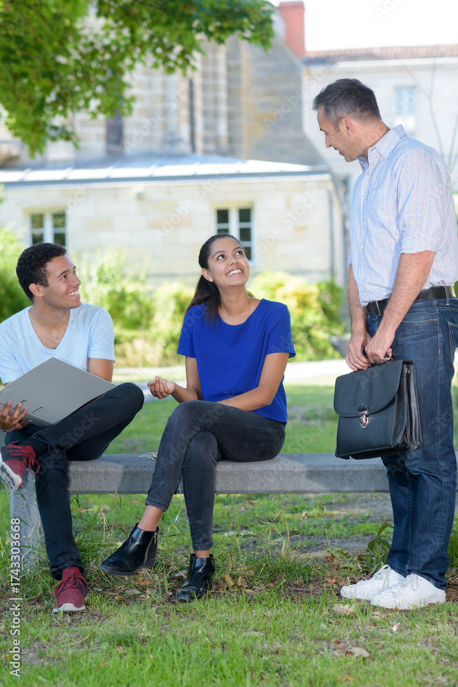 Fototapeta premium school teacher reviewing exercises with teenagers outside school