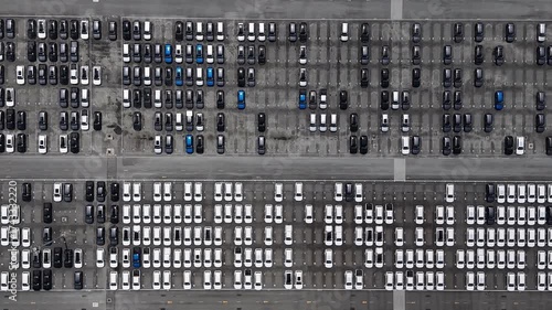 Aerial view of new cars in a large parking lot, arranged in geometric rows.