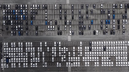 Aerial view of new cars in a large parking lot, arranged in geometric rows.