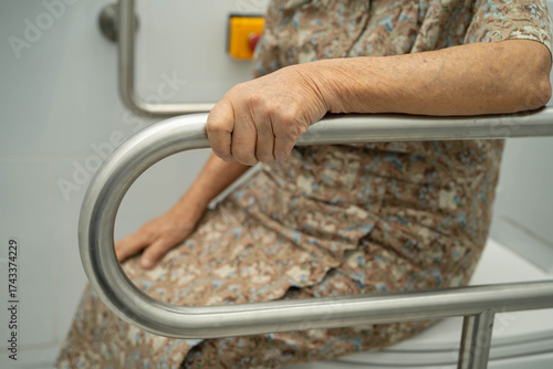 Asian elderly woman patient use toilet support rail in bathroom.