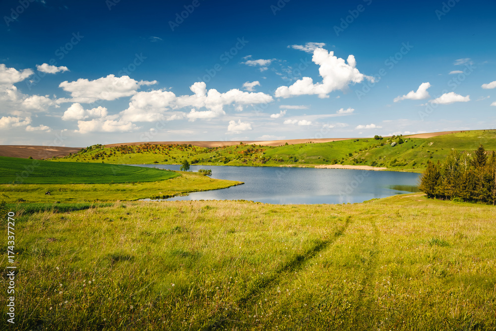 Obraz premium Breathtaking landscape with clear skies over a quiet lake and lush green hills on a sunny day. Gorgeous and atmospheric panorama, harmony and coziness. Photo wallpaper. Discovery the beauty of earth.