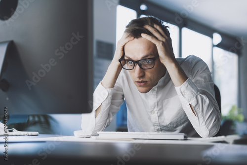 Insane stressed office worker sitting at desk with head in hands