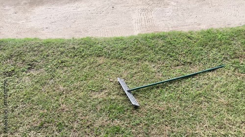 A green lawn mower is sitting on a patch of dry grass. The grass is brown and dry, and the mower is leaning against the ground. The scene gives off a sense of neglect and abandonment