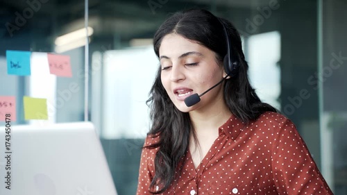 Young smiling female corporate operator in headset working in customer support service on helpline telesale talking using laptop in business office. Agent of call center advises client online Close up