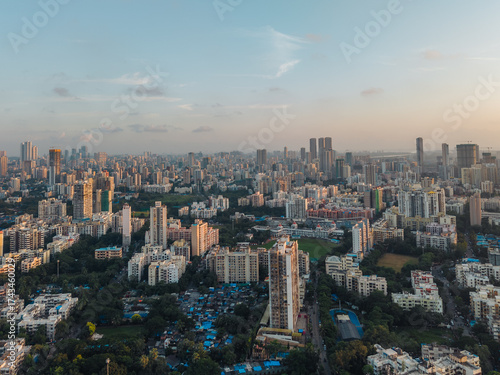 Aerial view of the densely packed cityscape, where concrete structures meet patches of green, all under the soft glow of twilight, Mumbai, Maharashtra, India.