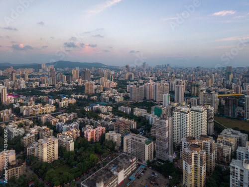 Aerial view of closely arranged buildings and green spaces bathed in the soft glow of twilight, casting long shadows across Mumbai's urban landscape, Mumbai, Maharashtra, India.