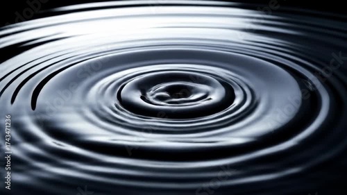 Water drop creating ripples on a dark liquid surface in motion.