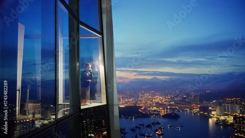 Mid adult businesswoman standing in a corporate windows with view of the city, talking on her mobile phone