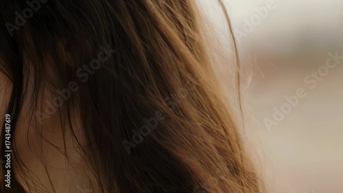 Close-up of long, wavy, brown hair, with a blurred background. Highlights and shadows play on strands
