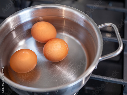 Obraz na płótnie Three brown eggs in a stainless steel pot on a gas stove with water, preparation for boiling hard boiled eggs in a home kitchen