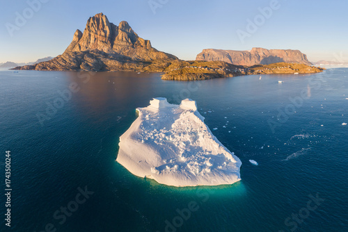 The mountain and island of Uummannaq with the village of the same name in western Greenland in one of the fjords. Floating icebergs, global warming, and climate change. Summer time, aerial view.