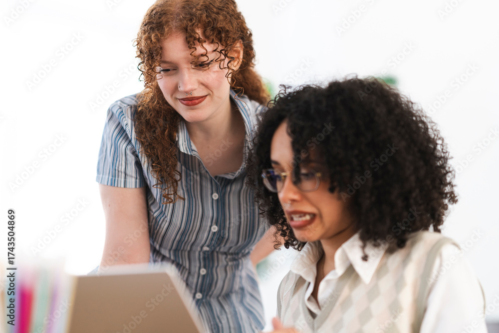 © Studio Marmellata - Two women collaborate on a project, looking at a laptop screen together in a bright, modern office setting.