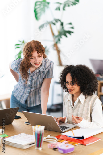 Two young women collaborate on a project, one typing on a laptop while the other leans in to discuss ideas.