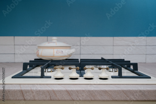 Close-up of a beige gas cooktop with a cast iron grate and a ceramic pot