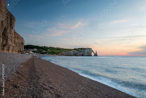 The beach of Etretat and the Porte d’Aval Cliff at sunset, natural rock arch and beach of the alabaster coast, department of Seine Maritime, Normandie region, France.