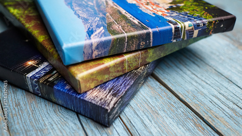 Three colorful canvas photo prints stacked on a rustic blue wooden surface, showing textured edges and vibrant printed landscapes