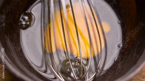 Raw egg yolk and white in ceramic bowl with metal whisk. Organic fresh protein baking ingredient