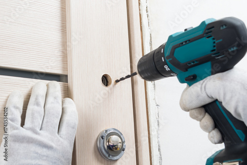 The master holds a screwdriver in his hands and makes holes in the door to install the door handle