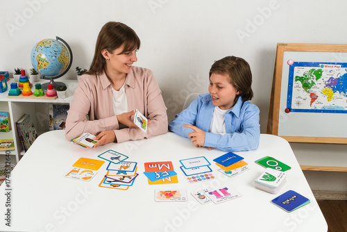 Happy teacher and young boy learning Spanish together with flashcards in a bilingual classroom. Concept of language development, communication, and fun education for kids.