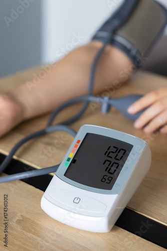Close-up of an automatic digital blood pressure monitor showing normal reading (120/70) during measurement on a patient’s arm. health check, hypertension prevention, heart care, and medical diagnostic