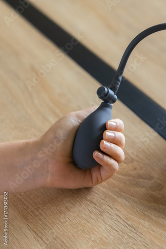 Close-up of a hand holding a rubber pump from a blood pressure monitor on a wooden table. Concept of self-care, medical diagnostics, hypertension prevention, and heart health monitoring.
