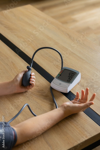 Person measuring blood pressure with digital tonometer and hand pump on wooden table. Concept of self-care, health monitoring, and hypertension prevention at home or in a clinic.