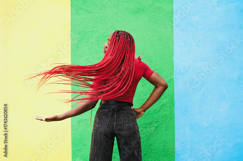 Woman with red braids posing playfully against colorful wall outdoors