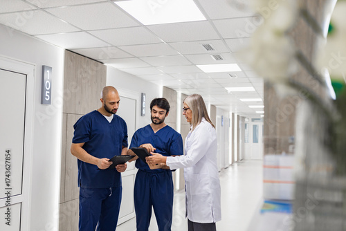A doctor and nurses review medical records in a clinic hallway, discussing patient care and treatment plans.