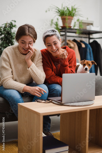 Content middle aged mother with young daughter laughing sincerely while chatting via laptop on sofa