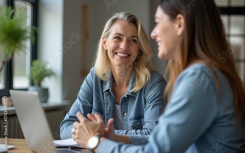 Positive mature businesswoman speaking to younger colleague in office coworking space, smiling, laughing, talking to employee, worker, giving advice for work on project. High quality