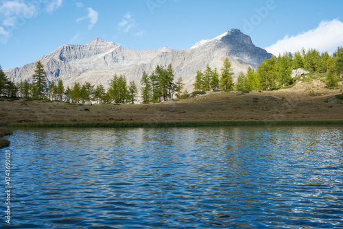 Panoramic view of Lake Dres in Gran Paradiso National Park, Piedmont, Italy. A sunny fall day with golden tones, snow-dusted peaks, and calm alpine reflections in a pristine mountain landscape