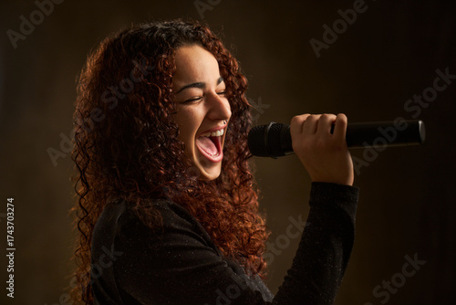 Woman with curly hair singing passionately into microphone