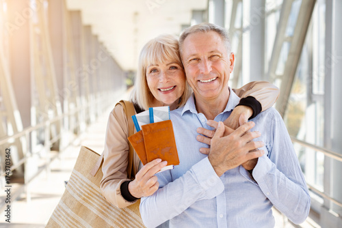 Smiling senior travelers embracing with passports and tickets at airport