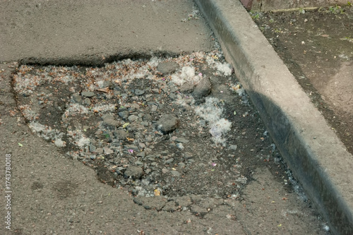 Asphalt road with a pothole, scattered clumps of poplar fluff on the surface, showing wear and outdoor detail.