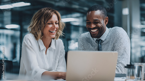 Two smiling colleagues look at a laptop screen in an office