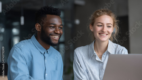 Two smiling professionals one Black man and one White woman looking at a laptop in an office setting