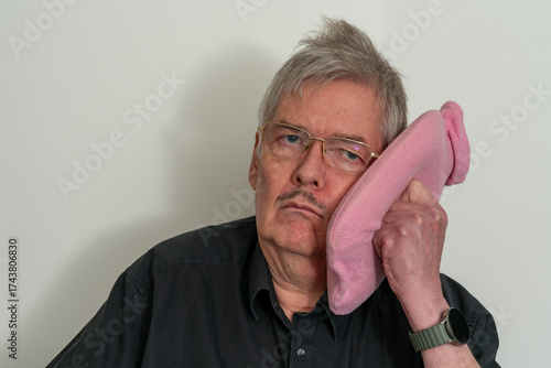Male having toothache and holding hot water bottle to his face, filled with hot or cold water. Unhappy look, White background. White space.