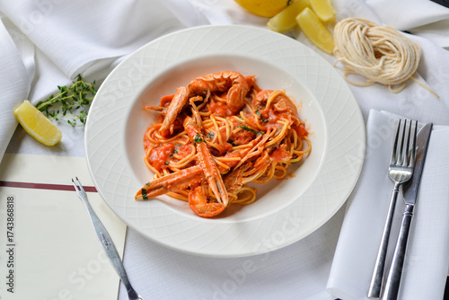 pasta with scampi in a white plate on a light background with lemon and cutlery