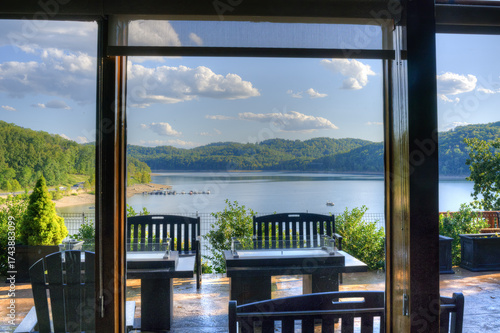 This photograph captures a serene lakeside view from what appears to be a covered patio or indoor space, looking out through large windows or open doors