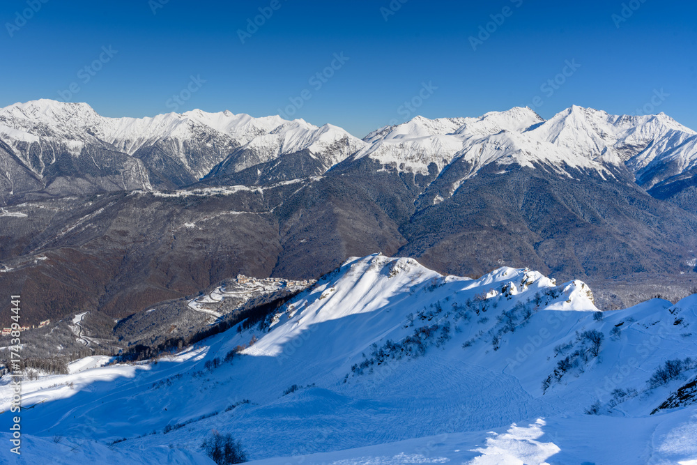 Obraz premium Mountainside, valley. In the background there are beautiful snow-capped mountains and an opening view of the valley. The bright winter sun highlights the snow-white landscapes.