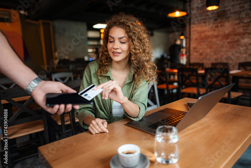 Young woman paying with credit card using contactless payment in cafe