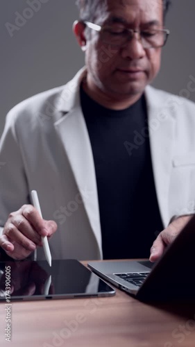 Mature male professional working digitally. Expert designer creates content using stylus, tablet, laptop. Focused individual develops innovative solutions. Business, education, healthcare concepts.