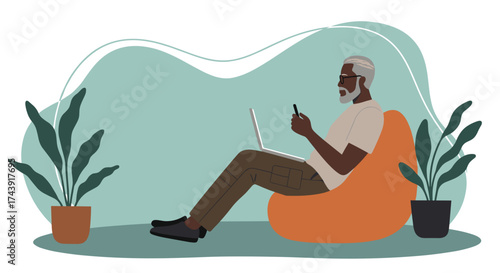 Black senior man using laptop and phone on bean bag Remote work online leisure digital lifestyle
